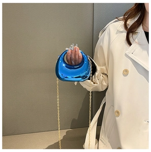 Mini crescent acrylic bag in electric blue worn with golden chain over a beige coat