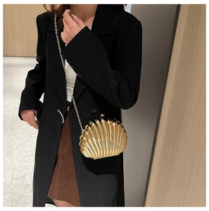 Elegant gold shell evening bag with metal chain strap styled on a minimalist black suit