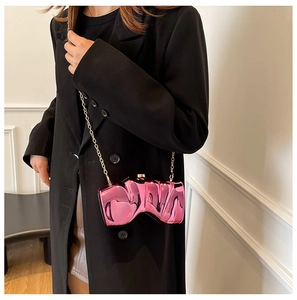 Macro shot of stylish pink metallic wave-shaped clutch bag with golden chain strap