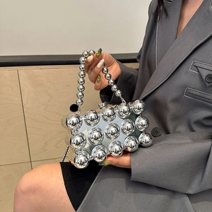 Futuristic silver spherical evening bag with polished bead handle held by a model