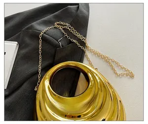Detail of a liquid metal texture gold clutch bag with a sleek round handle and chain strap