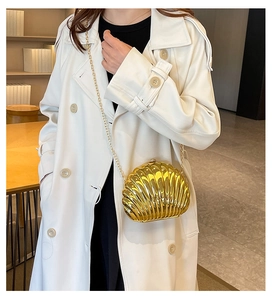 Detail of a metallic gold shell-shaped clutch bag with fine metal chain on white coat