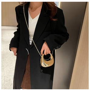 Mini gold crescent evening bag with metallic chain strap worn over a black blazer