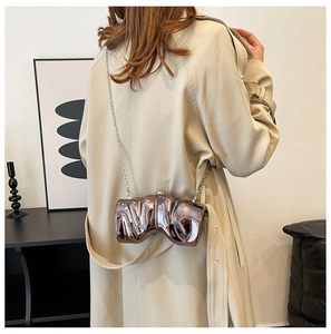 Detail view of a bronze-toned fluid metal evening clutch worn with a beige trench coat