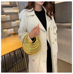 Close-up of a gold metallic crescent clutch bag with pleats and chain on a white coat