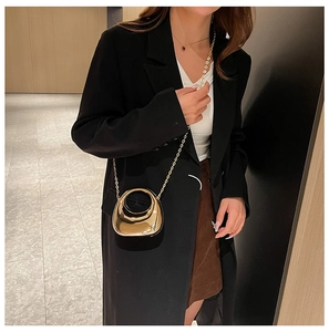 Close-up of a gold semi-circular acrylic clutch with chain strap on a black blazer