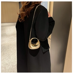 Detail of a gold metallic half-moon bag with round handle and gold chain strap on black suit