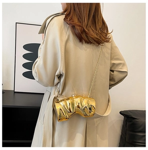 Detailed view of a gold fluid-shaped evening clutch bag on a beige trench coat