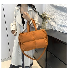 Detail of bright orange quilted tote bag featuring padded handles and a spacious design