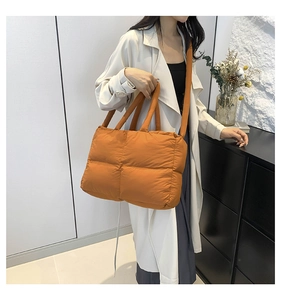 Detail of orange quilted nylon tote bag with thick handles worn by a model in a white coat