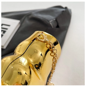 Macro detail of gold-plated box clutch featuring polished wing design and chain link attachment