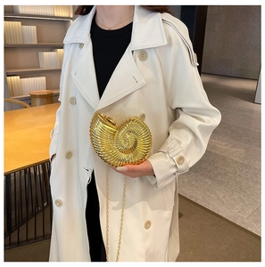 Detail der goldenen Muschel-Clutch mit Metallic-Textur auf weißem Trenchcoat-Stil