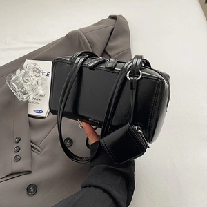 Minimalist black patent leather shoulder bag with a mini pouch in a lifestyle setting