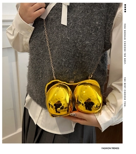 Detail of creative gold mirrored bra-shaped clutch bag with long metal chain strap