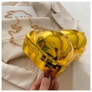 Close-up of a gold mirror-finish artistic bag with a thin metal chain strap on beige suit