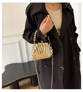 Golden shell-shaped evening clutch bag with beaded handle worn on a black coat