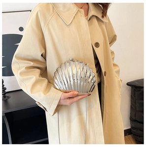Detail of silver shell-shaped evening bag with metal chain strap on beige trench coat