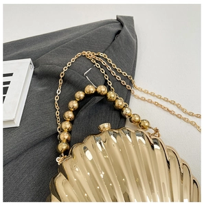 Detail of golden shell-shaped evening bag with rippled texture and beaded handle