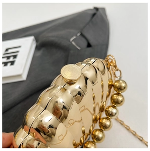 Macro detail of the golden shell evening bag with mirror bead chain and wavy texture