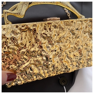 Details der goldenen Abendtasche mit plissierter Metalltextur und Skulpturengriff