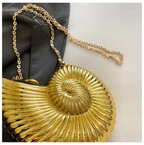 Detail of a golden conch-shaped evening clutch bag with spiral textures and chain strap