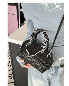 Primer plano detallado de bolso negro brillante con grabado de cocodrilo y serpiente.