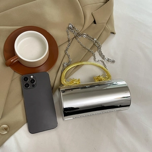 Sac de soirée cylindrique miroir argenté avec poignée en métal dragon doré sur table
