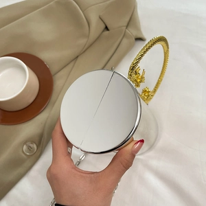 Détail d'un sac de soirée cylindrique avec poignée dragon dorée et corps en argent poli