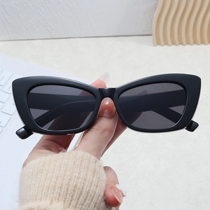 Close-up of black cat-eye sunglasses with dark lenses held over a desk setup