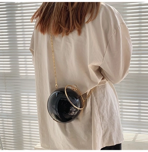 Detailed view of glossy black spherical crossbody bag with golden chain and ring handle