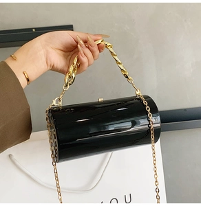 Detail of black acrylic cylindrical evening bag with gold chain and glossy finish