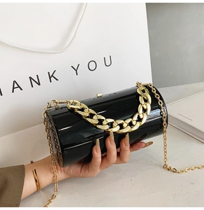 Detail of glossy black cylindrical clutch with decorative thick gold chain strap
