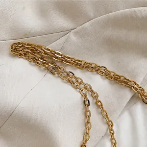 Close-up of polished gold metal chain strap on a textured beige blazer fabric