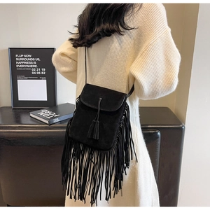 Détail du sac bandoulière bohème en daim noir avec de longues franges sur un pull blanc