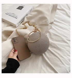 Detail of a champagne round evening bag with metal ring handle and chain strap