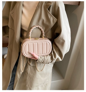 Detail of nude pink acrylic box bag with braided handle and gold chain on trench coat