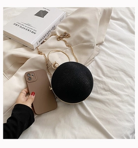 Spherical black evening bag with gold ring handle and chain strap on soft fabric