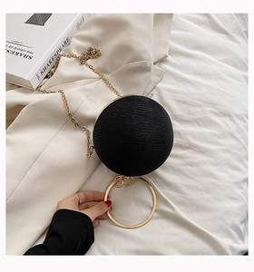 Detail of black spherical evening bag with metal ring handle and gold chain on fabric