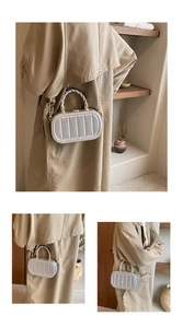 Detail of silver hard-shell crossbody bag featuring vertical stripes and a gold chain strap