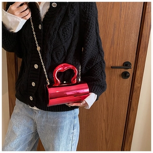 Detail of red metallic cylindrical clutch bag with artistic handle and gold chain strap