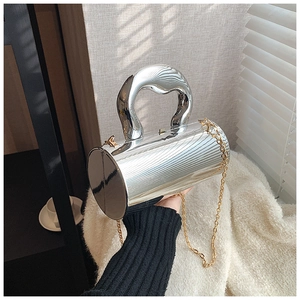 Close-up of silver cylindrical evening bag with sculptural handle and gold chain strap