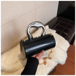 Detail view of black cylindrical evening bag with silver wavy metal handle and gold chain