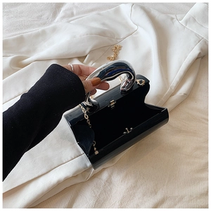 Detail of black acrylic box evening bag with silver liquid-metal handle and gold chain