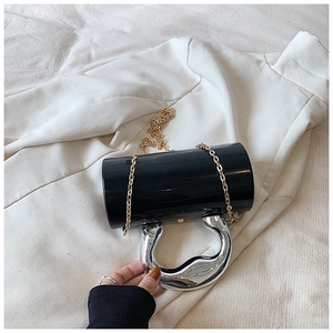 Close-up of black acrylic cylinder bag with liquid metal silver handle and gold chain