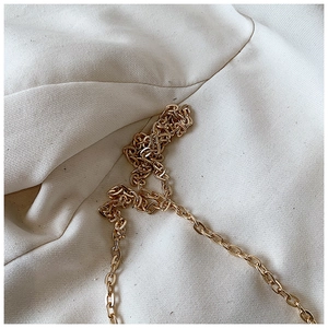 Close-up of a high-gloss gold metal chain strap on white textured fabric background