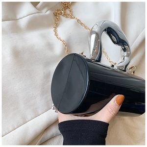 Detail of a black glossy cylindrical evening bag with large silver metal handle and chain