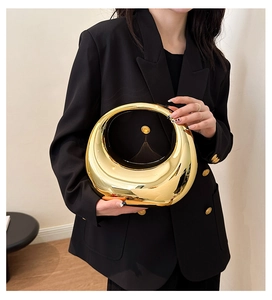 Chic gold crescent-shaped metal clutch bag with mirror finish held by model in black suit