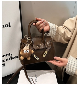 Detail of dark brown leather handbag with gold twist lock and plush monster charm decoration