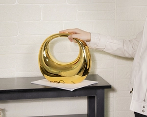 Nahaufnahme der goldenen ovalen Clutch mit glänzendem Spiegeleffekt und Metalltextur