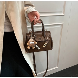 Detailed view of deep brown mini tote with gold hardware and plush monster charm charm